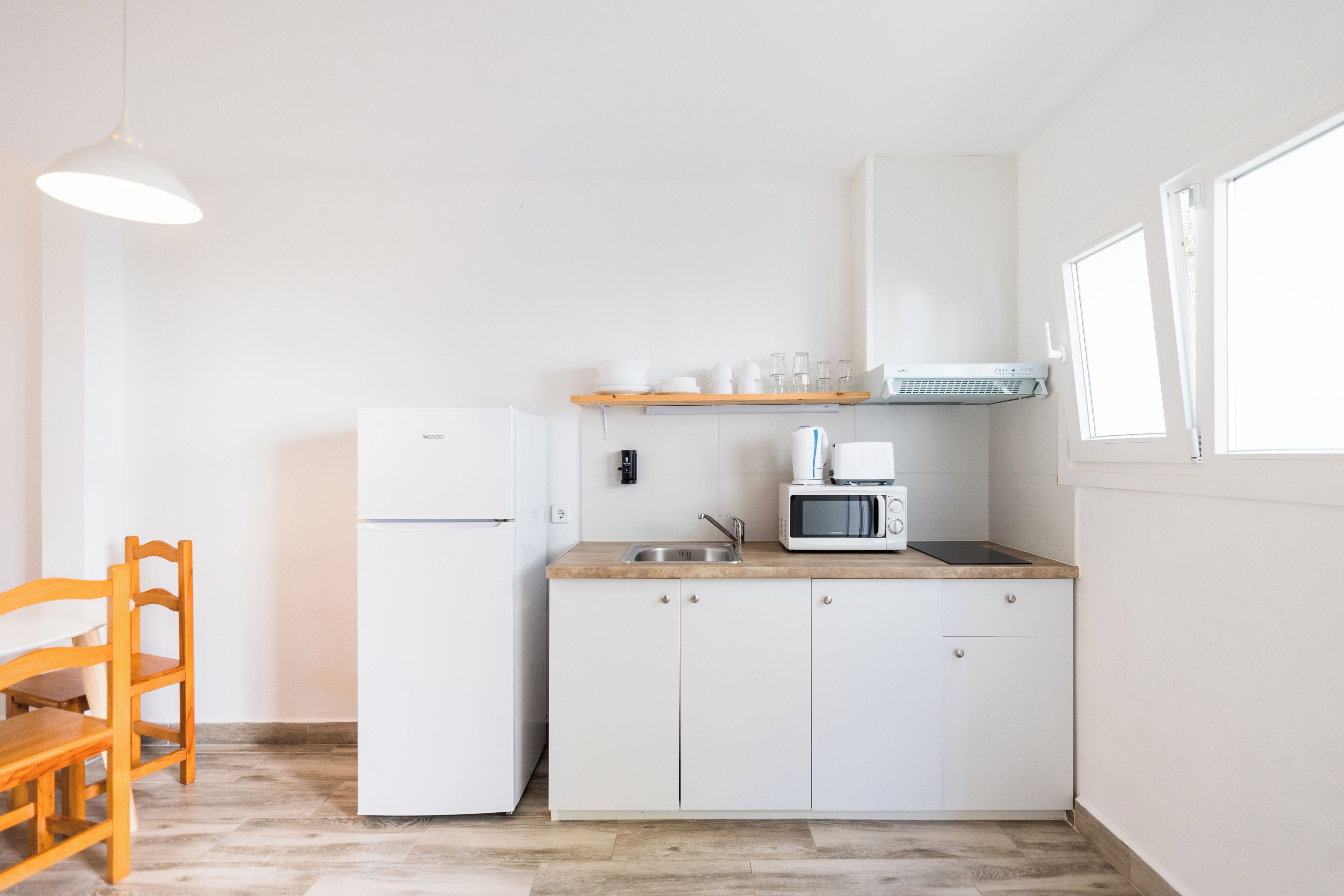 A compact kitchen with a refrigerator, microwave, and a wooden chair.