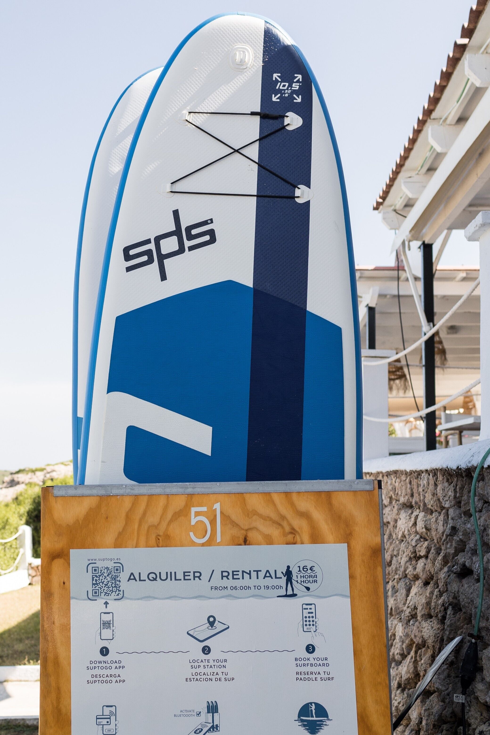 A surfboard with the text 'sps' and a rental sign with instructions for using the Suptogo app.