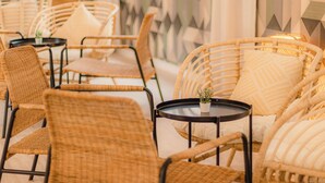 Wicker chairs and tables arranged in a seating area with a geometric patterned wall in the background. - Aparthotel Sol Parc (Mercadal)