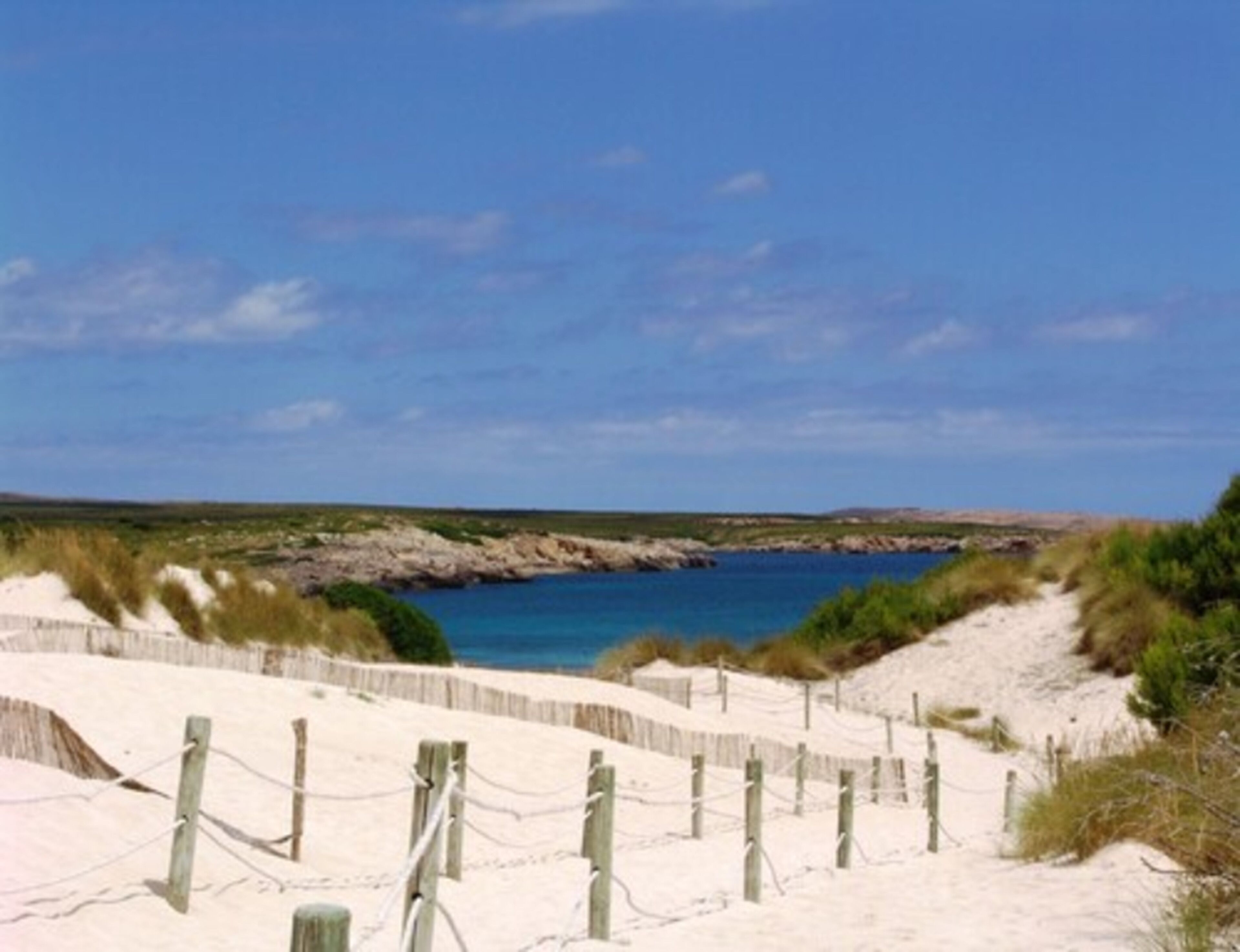 Une plage de sable bordée d’une clôture en bois, sous un ciel bleu et dégagé.
