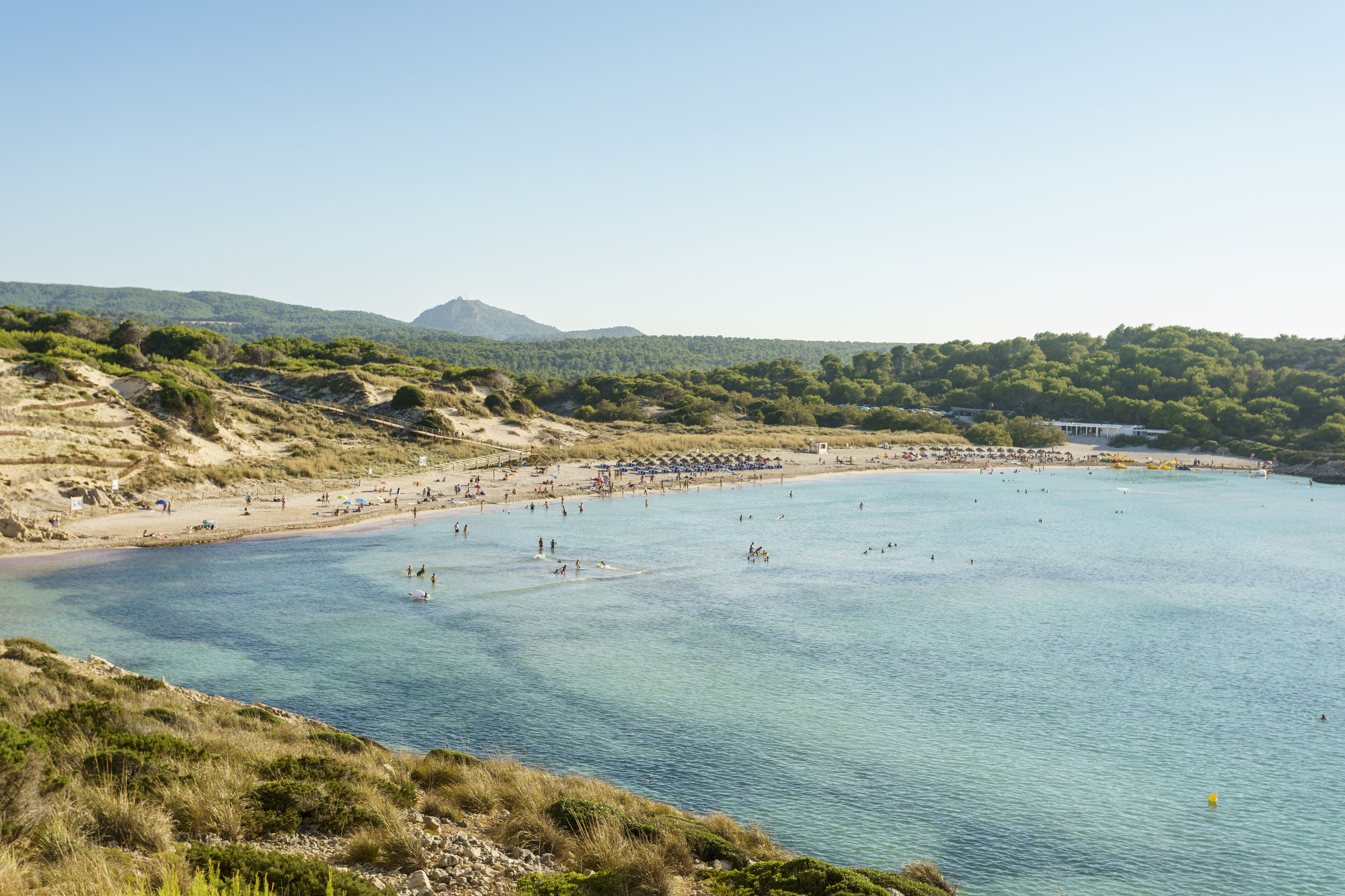 A coastal beach with clear waters, sandy shores, and a mountainous backdrop.