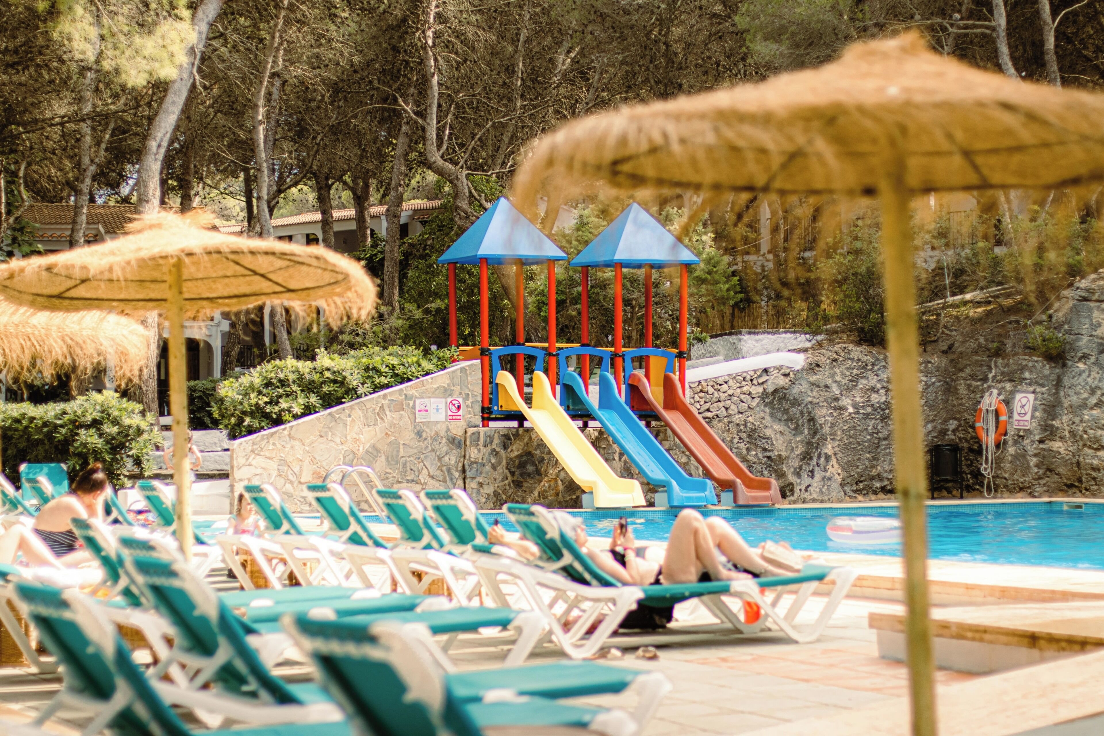 Un espace piscine équipé de chaises longues, de parasols et d’un toboggan.