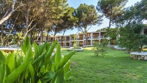 A hotel courtyard with a well-maintained lawn, a stone pathway, and a building with multiple balconies. - Aparthotel Sol Parc (Mercadal)