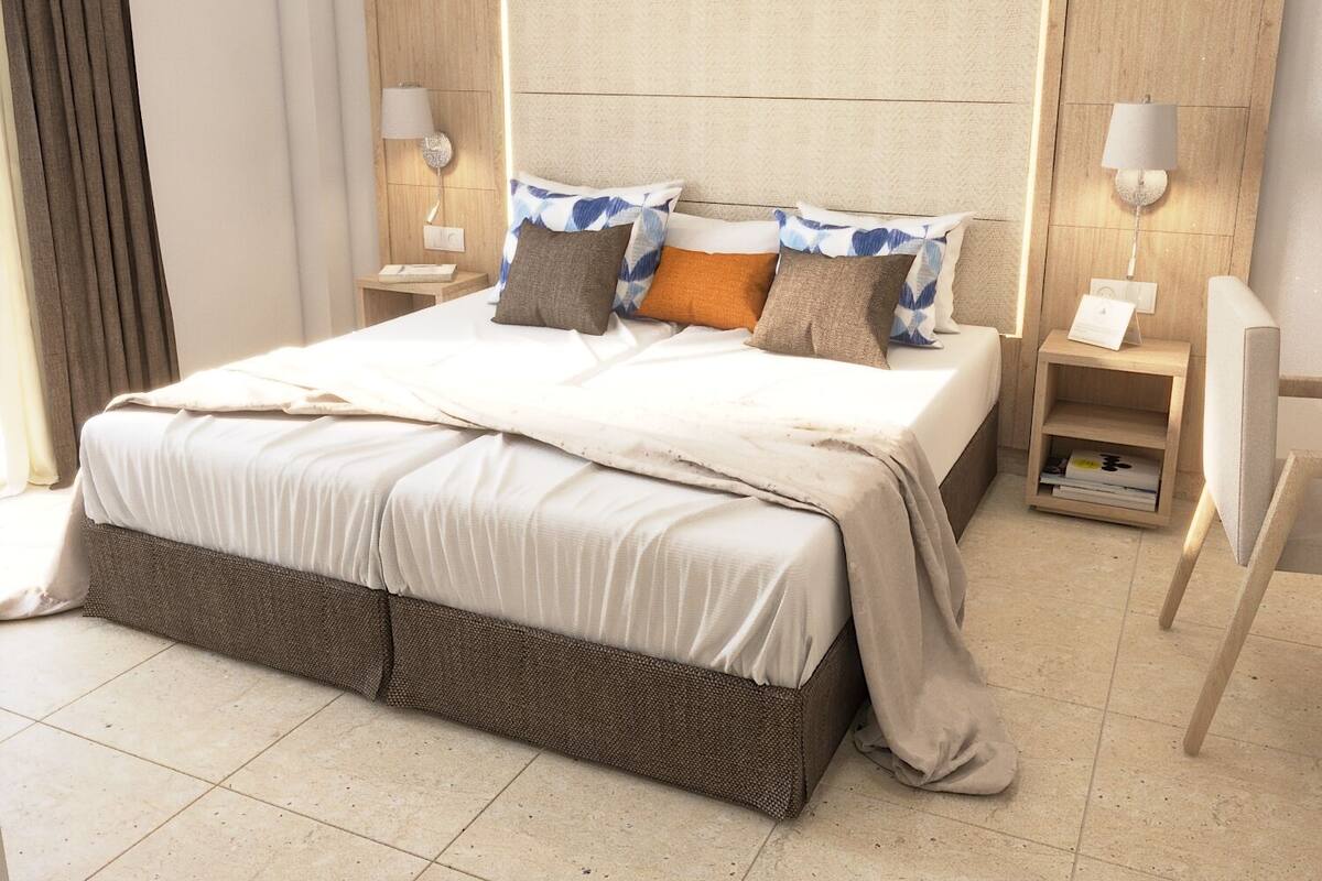 Een keurig opgemaakt bed met een hoofdbord, twee nachtkastjes met lampen, en een rieten voeteneind.