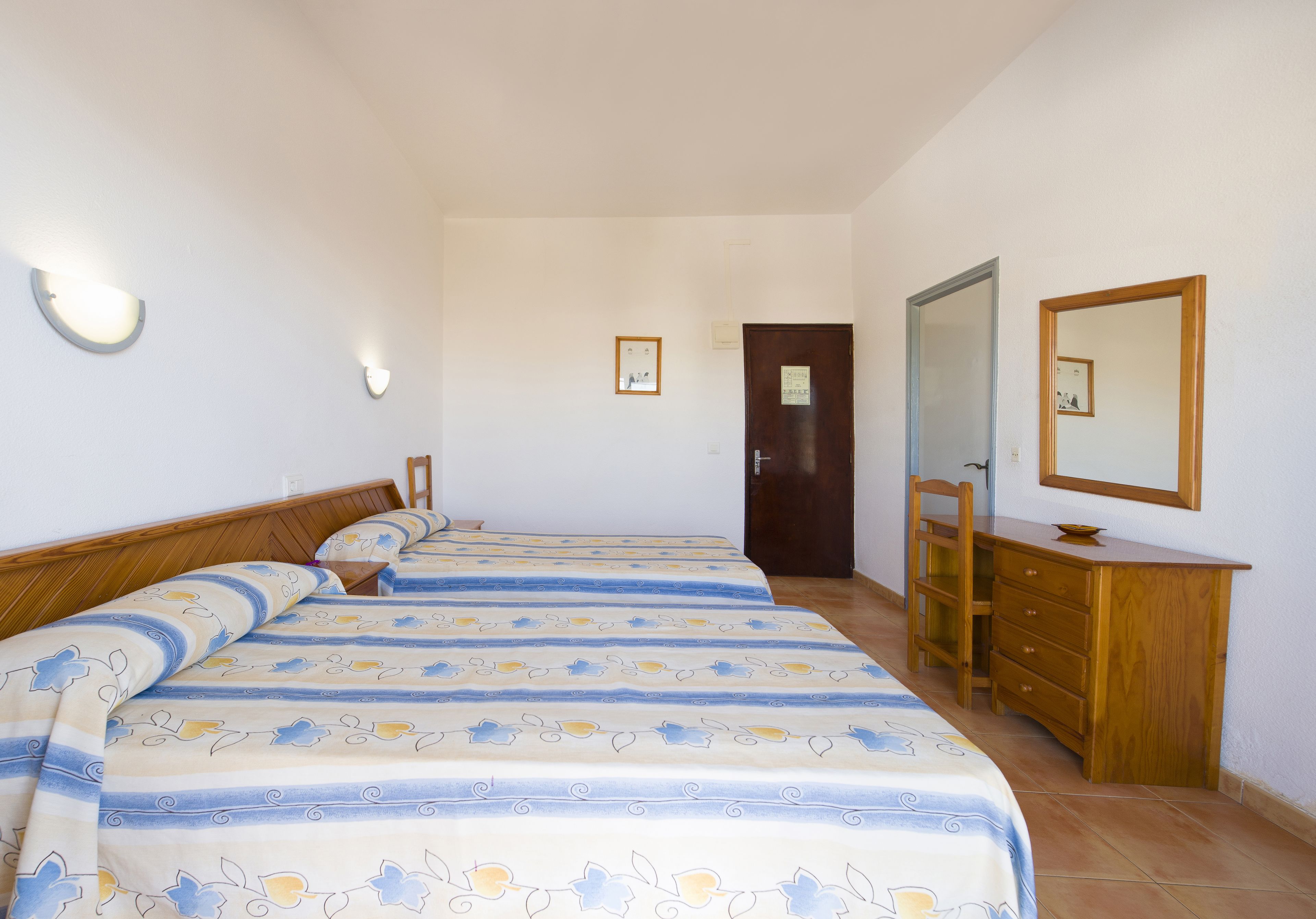 A bedroom with two beds, a wooden dresser, a mirror, and a door.