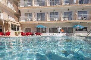 Una piscina con una decoración de cisne, sillas rojas y sombrillas.