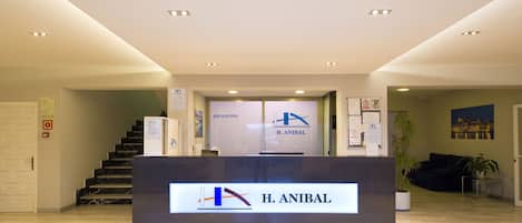 A reception area with a reception desk labeled "H. Anibal," a staircase, and a potted plant.