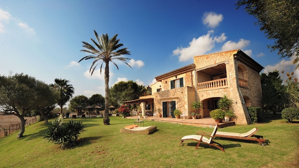 Une villa en pierre dotée d’un balcon, entourée d’une pelouse bien entretenue et de palmiers.