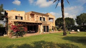 Une maison en pierre à deux étages, dotée d’un balcon, d’une terrasse avec mobilier d’extérieur et d’une pelouse bien entretenue.