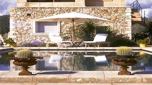 Un bâtiment en pierre avec une piscine, deux chaises longues et un parasol.