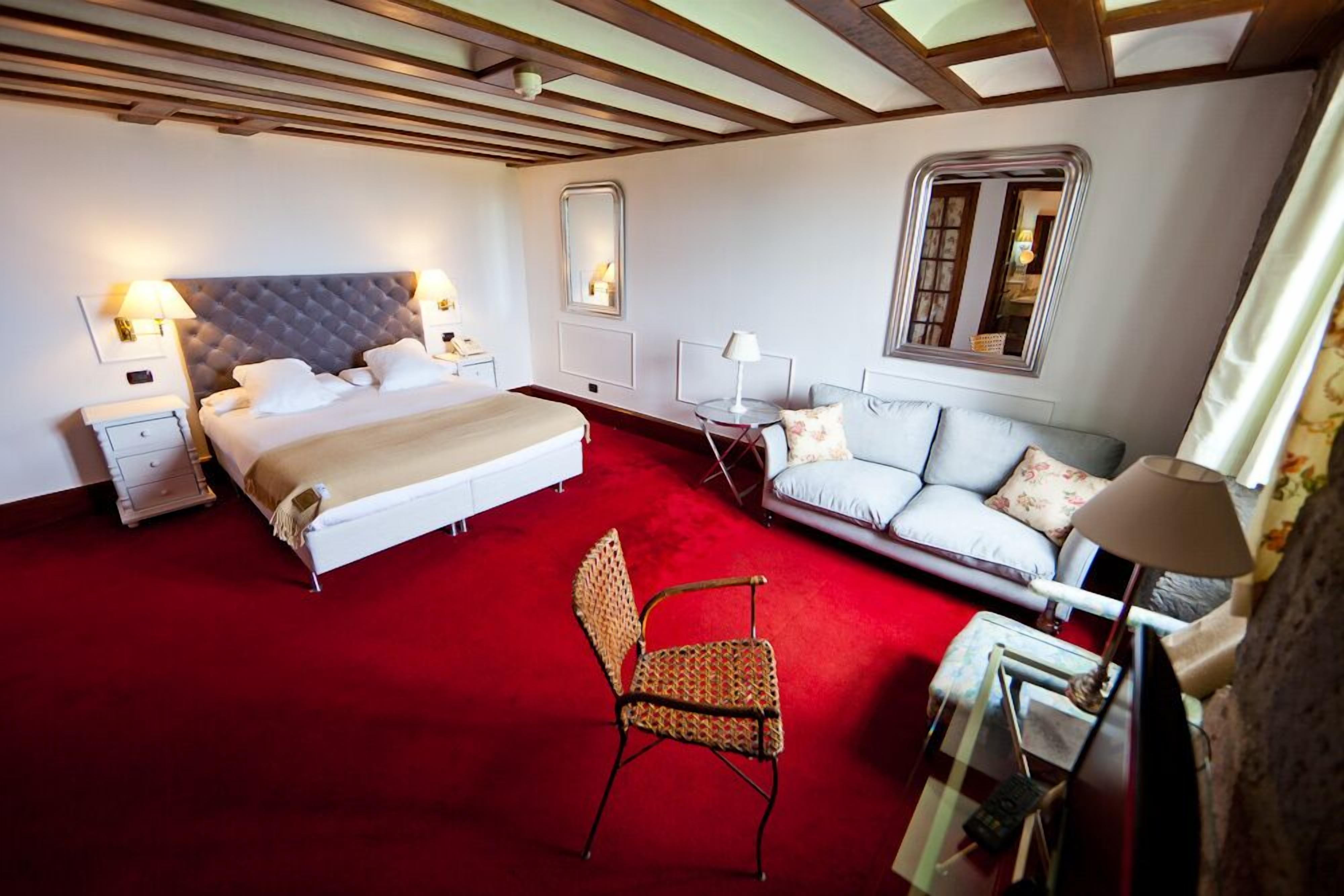 A hotel room with a large bed, a sofa, a chair, and a desk with a lamp.