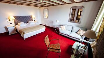 A hotel room with a large bed, a sofa, a chair, and a desk with a lamp.