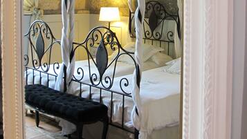A bedroom with a four-poster bed, a nightstand, and a mirror reflecting the room.