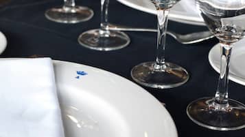 Una mesa servida con platos blancos, copas de vino transparentes y un tenedor plateado.
