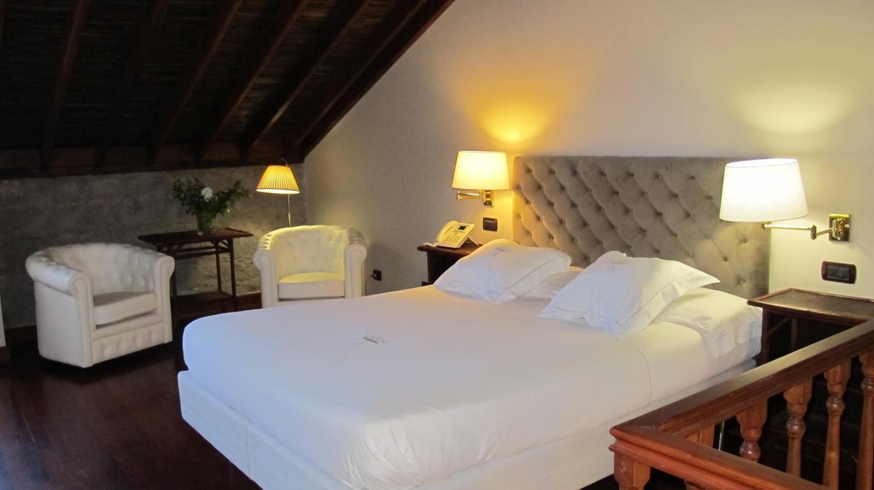 Une chambre d’hôtel avec un grand lit, deux lampes de chevet, un téléphone, une petite table avec une lampe et une chaise.