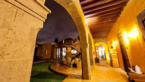 Pátio interior com arcos de pedra, teto de madeira e um caminho bem iluminado.