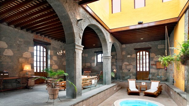 Um pátio com hidromassagem, arcos de pedra, móveis de madeira e plantas em vasos.