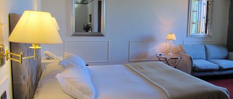A hotel room with a bed, two bedside lamps, a chair, and a window.