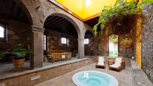 Área interna de piscina com paredes de pedra, bancos de madeira e espreguiçadeiras.