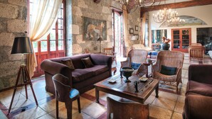 Uma sala de estar ampla com paredes de pedra, vigas de madeira, um candelabro e assentos confortáveis.
