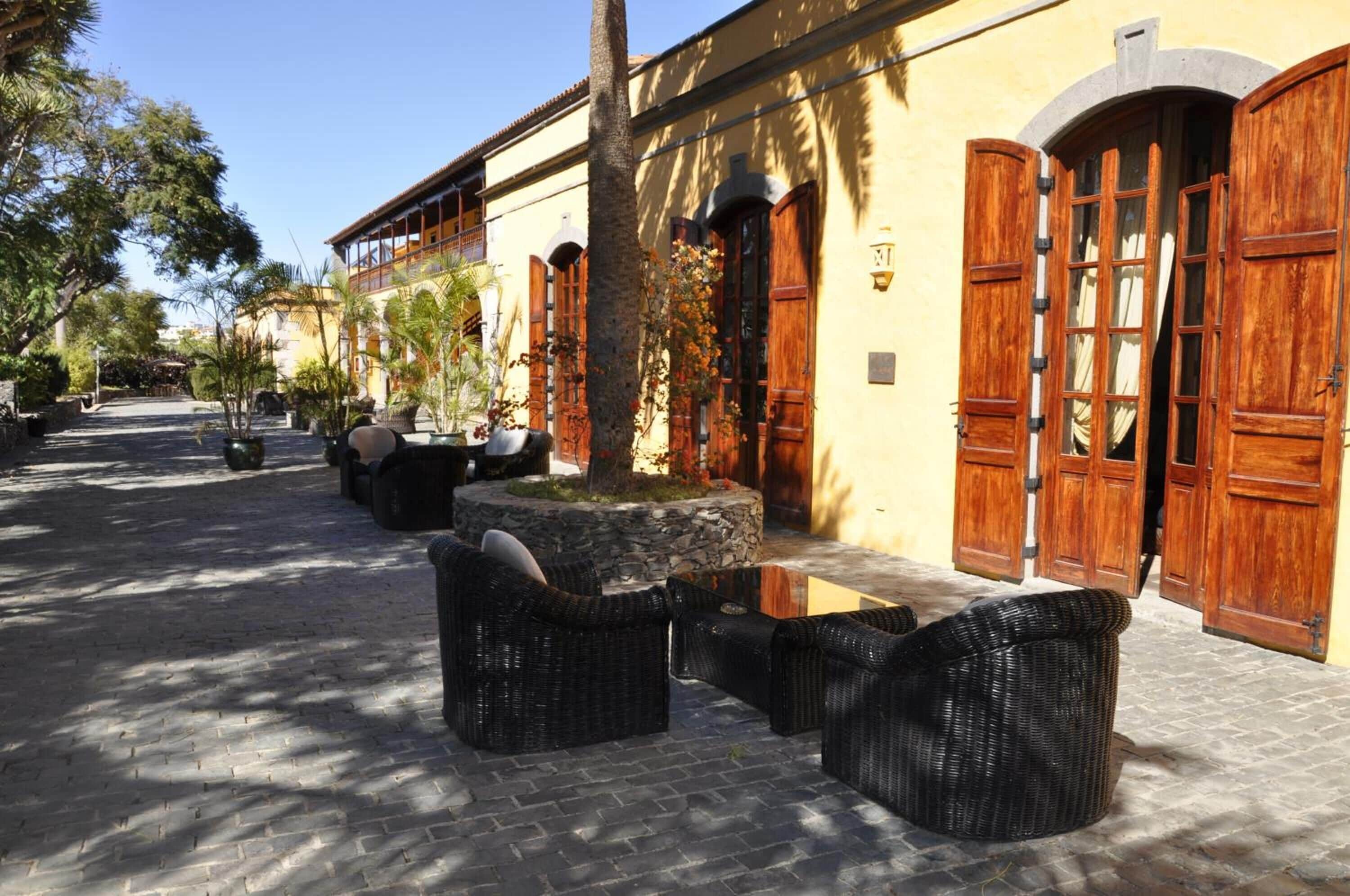 Un patio con mobiliario de mimbre, macetas de piedra y puertas de madera.