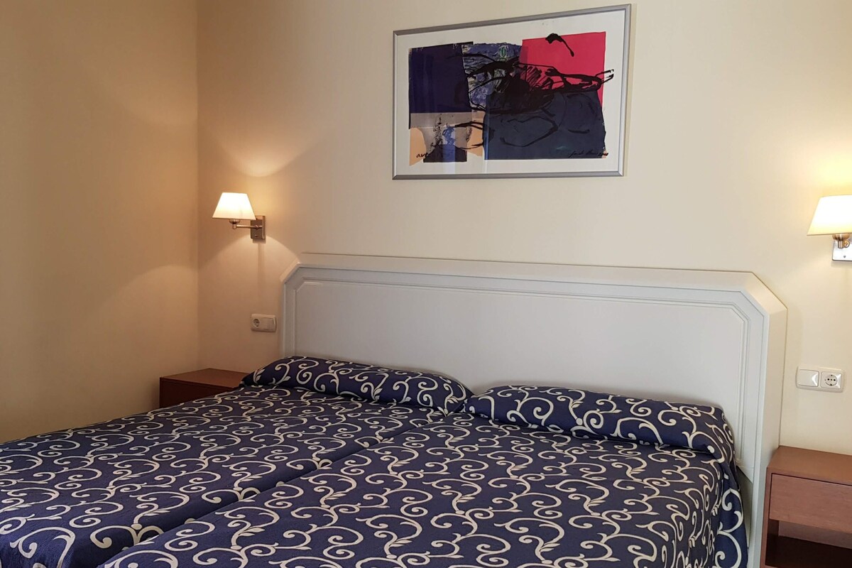 A neatly made bed with a patterned bedspread, two bedside lamps, and a framed abstract artwork above the bed.