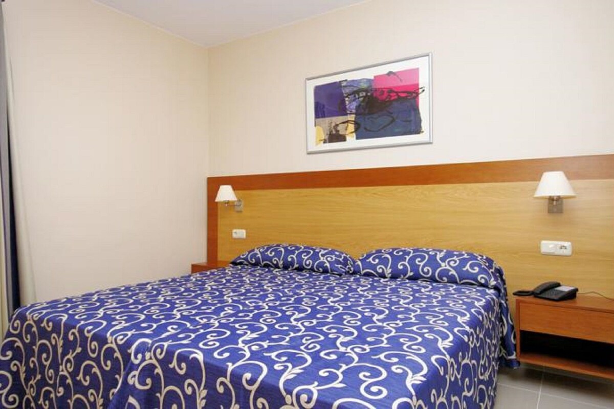 A hotel room with a bed, two bedside lamps, a nightstand, a telephone, and a framed picture on the wall.