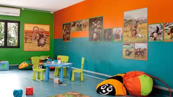 A brightly colored children's playroom with green and orange walls, a blue carpet, and various toys and educational materials.
