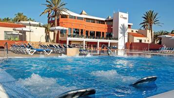Una piscina con delfines, sillones de descanso y un edificio de fachada roja.