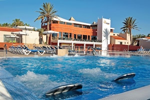 Una piscina con delfines, sillones de descanso y un edificio de fachada roja.