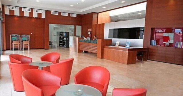 Eine moderne Lobby mit roten Sitzgelegenheiten, einem Empfangsbereich und einem großen Fernsehbildschirm.