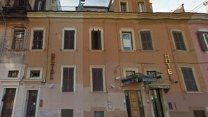 Un edificio de varios pisos con un letrero que indica que es un hotel. Tiene varias ventanas con persianas y un estilo arquitectónico tradicional.