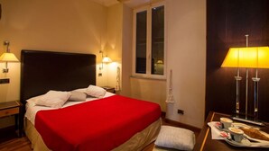 Habitación de hotel con cama, lámparas de noche, ventana, mesita de noche y bandeja con croissant y café.
