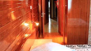 A hotel room with wooden paneling, a bed with patterned bedding, and a door leading to another room. - Mindel Hotel (São Vicente)