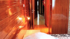 Habitación de hotel con paneles de madera, una cama con ropa de cama estampada y una puerta que conduce a otra habitación.