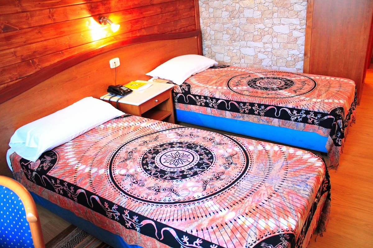 A room with two beds, each with a patterned bedspread, a wooden headboard, a stone wall, and a wooden floor.