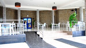 A spacious lobby with a stone wall, a reception desk, and a staircase leading to upper floors. - Mindel Hotel (São Vicente)