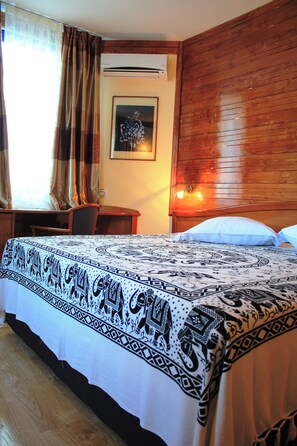 A hotel room with a bed, a desk, a chair, a window with curtains, an air conditioning unit, a wall-mounted lamp, and a framed picture on the wall. - Mindel Hotel (São Vicente)