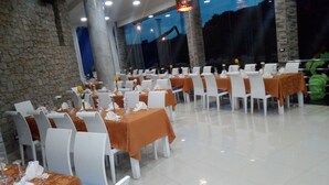 A dining area with tables set for a meal, white chairs, and a stone wall in the background. - Mindel Hotel (São Vicente)