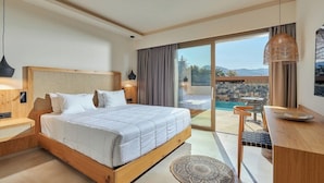 A modern hotel room with a large bed, a desk, a chair, a small table, a hanging light fixture, and a view of a pool and mountains. - Lambi (Malevizi)