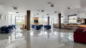 A spacious lobby with high ceilings, large windows, and a bar area. - Lambi (Malevizi)