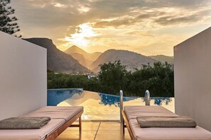 A poolside area with two lounge chairs, a clear view of mountains, and a sunset.