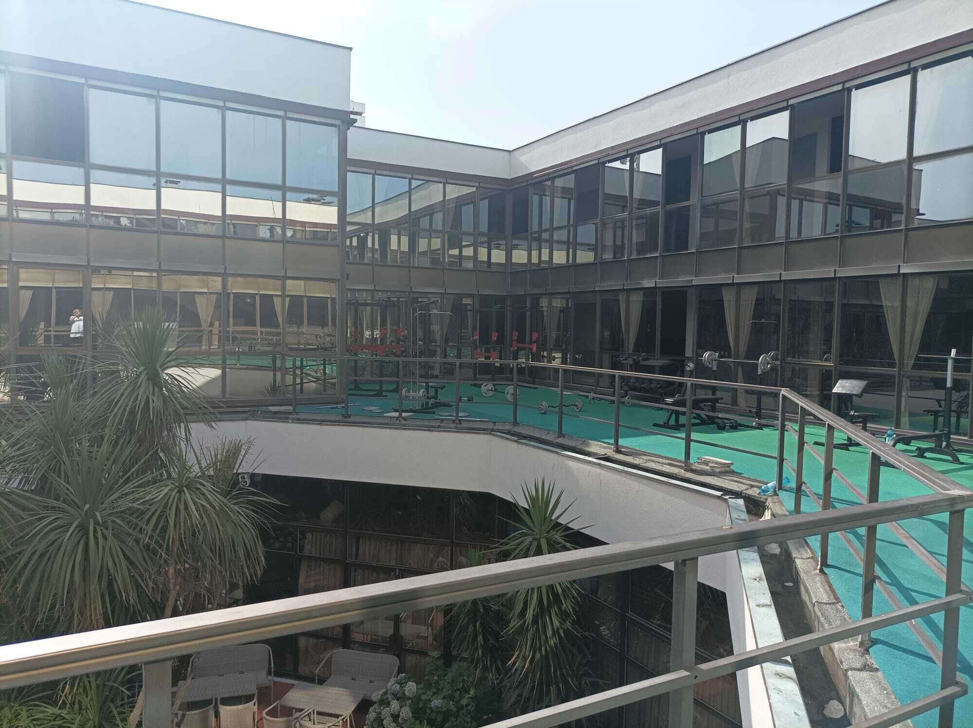 A multi-level indoor swimming pool with glass walls, surrounded by potted plants and gym equipment.