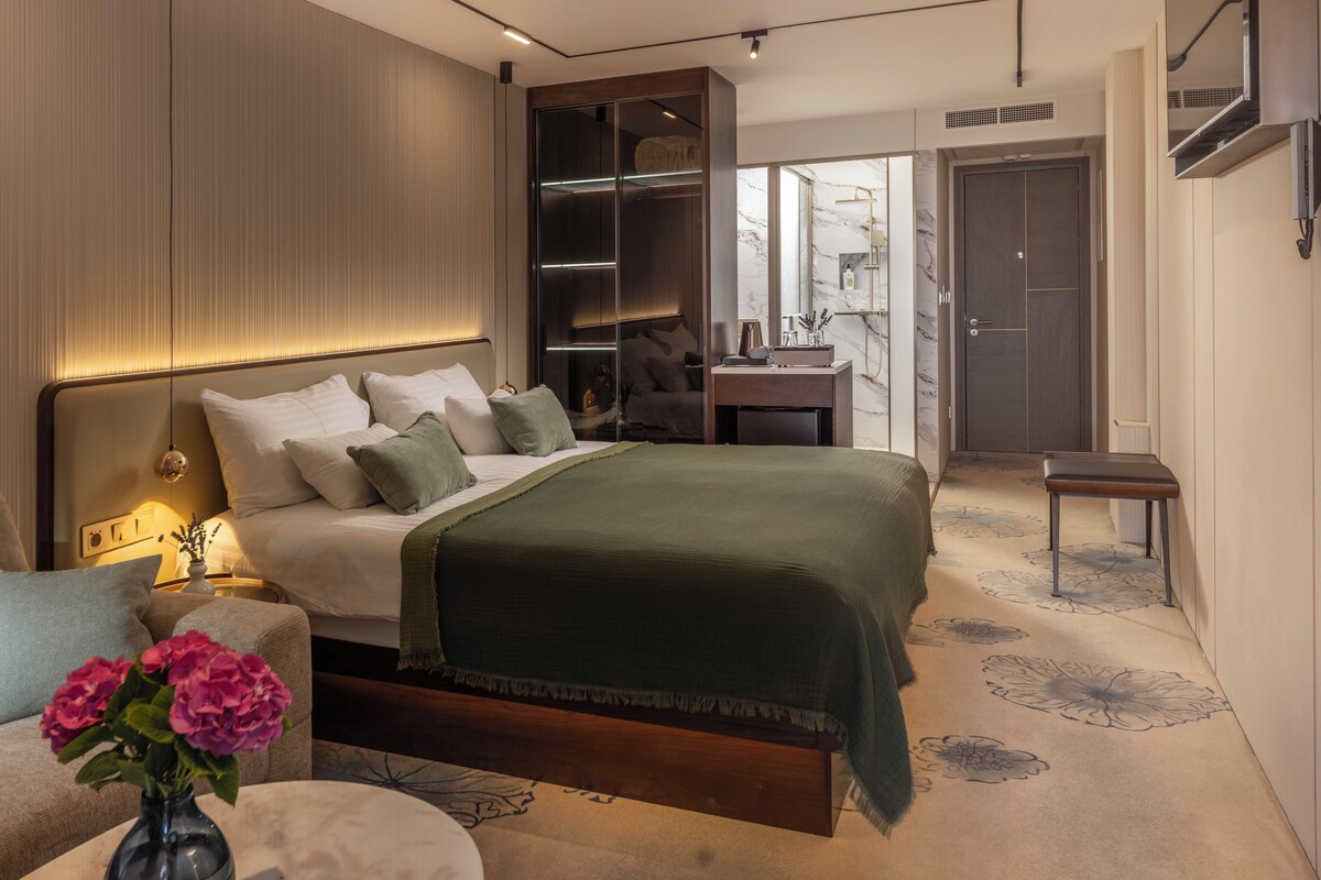 A modern bedroom with a large bed, bedside tables, a nightstand, a dresser, and a walk-in closet.