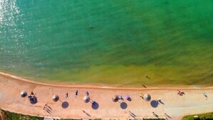 An aerial view of a beach with clear water, a sandy shore, and several umbrellas and people. - Hotel Liberty (Novalja)