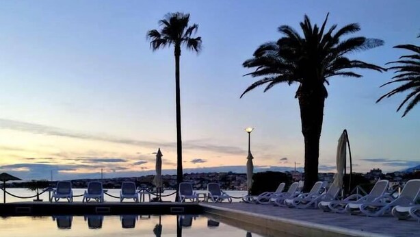 A tranquil pool area with lounge chairs and palm trees, reflecting the sky and surrounding landscape. - Hotel Liberty (Novalja)