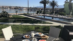 A table set with breakfast items, overlooking a pool and a scenic view of a coastal town. - Hotel Liberty (Novalja)