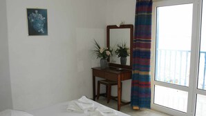 Quarto com cama, escrivaninha, cadeira, espelho, planta em vaso e janela com vista.