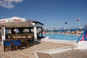 A poolside area with a Coca-Cola branded umbrella, a bar, and lounge chairs.