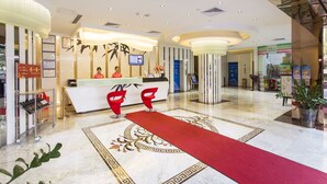 Un hall d'hôtel avec un comptoir d'accueil, deux fauteuils rouges, une moquette rouge et un motif décoratif sur le sol.